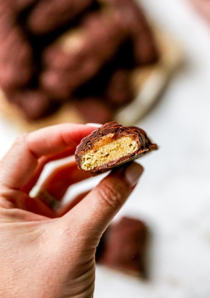 A hand holding up half of a healthy twix bar, exposing the inside cookie layer with date caramel sauce.