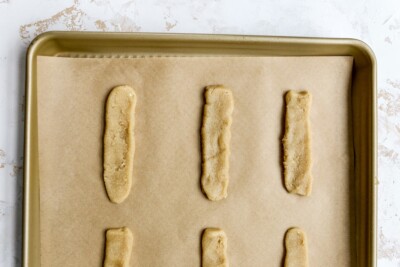 Cookie dough shaped into thin wafers in a row on a sheet pan.