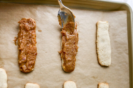 Baked wafer cookies being topped with date caramel layer on a baking sheet lined with parchment paper.