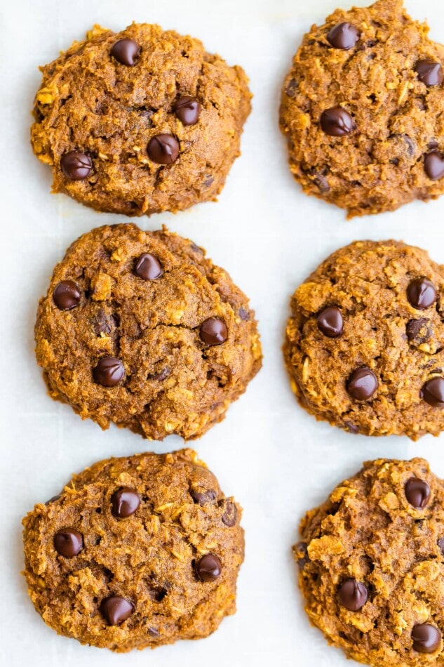 A close up of 6 baked pumpkin oatmeal cookies on a sheet of parchment paper.