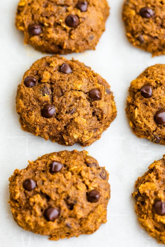 A close up of pumpkin oatmeal cookies, fresh from the oven. The cookies are resting on a sheet of parchment paper.