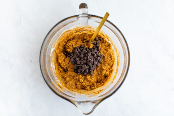 Mixing bowl with chocolate chips resting on top of cookie dough. A golden spoon rests inside the bowl.
