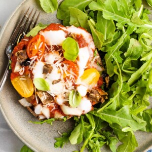 Close up, overhead shot of a portobello mushroom pizza plated with arugula. A silver fork rests on the plate.