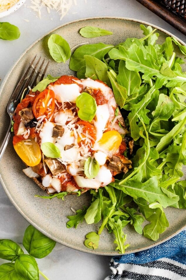 Close up, overhead shot of a portobello mushroom pizza plated with arugula. A silver fork rests on the plate.