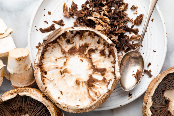 A portobello mushroom cap with its gills removed. A silver spoon rests on the plate with the gills that have been removed.