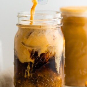 A mason jar with cold brew coffee and pumpkin cream being poured in. The cream is mixing in with the cold brew.
