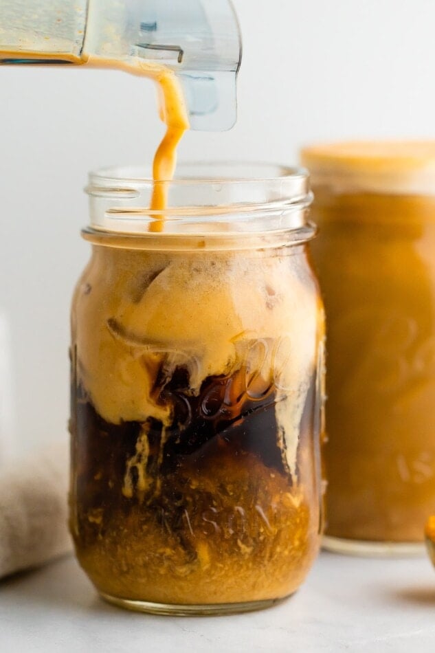 A mason jar with cold brew coffee and pumpkin cream being poured in. The cream is mixing in with the cold brew.