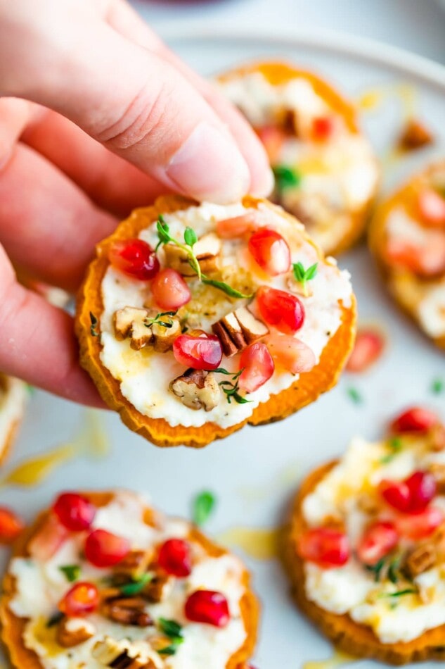 A hand is holding up a sweet potato bite, with additional sweet potato bites on a plate underneath and out of focus.