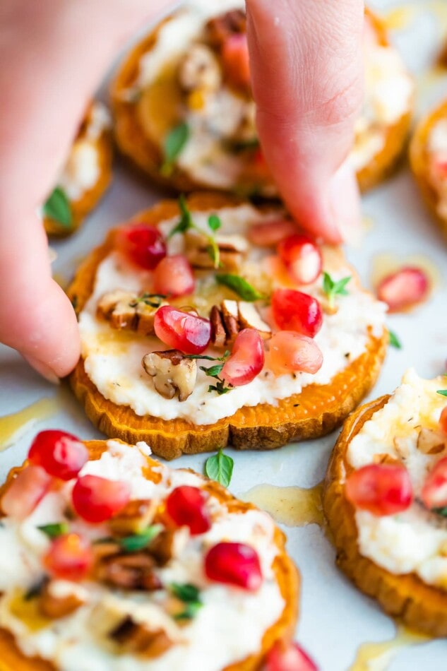 A hand grabbing a single sweet potato bite from a plate.