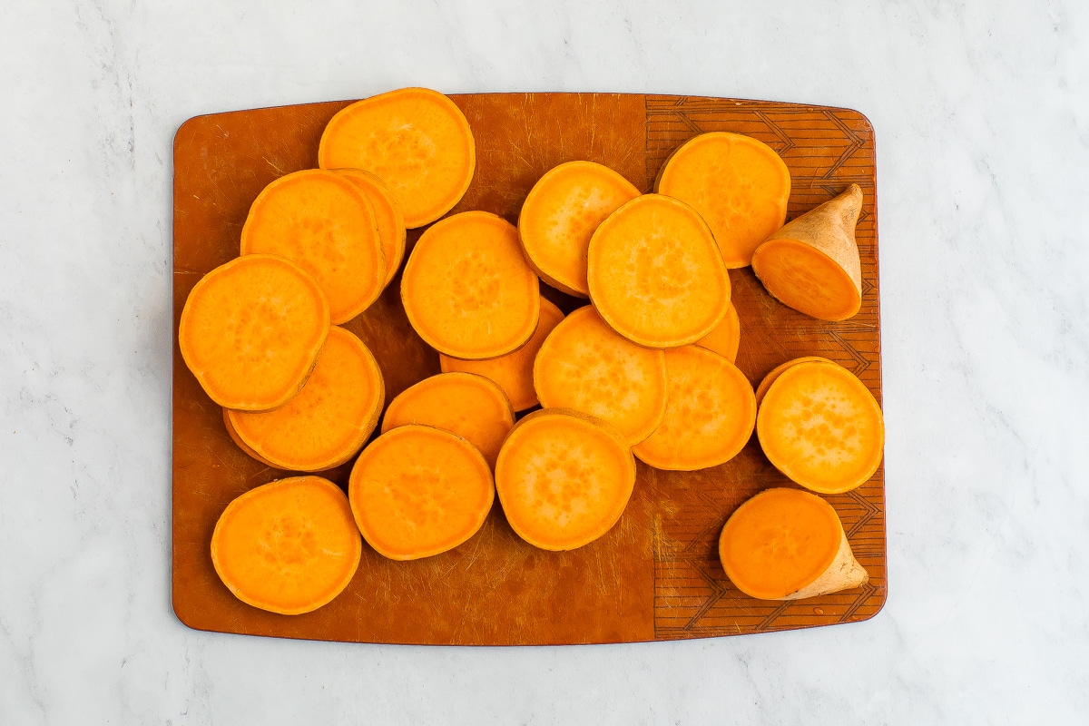 A chopping board with sweet potato chopped into rounds.