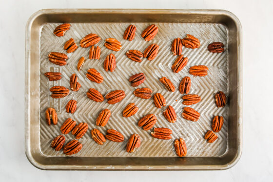 A sheet pan scattered with pecans, ready to be roasted.