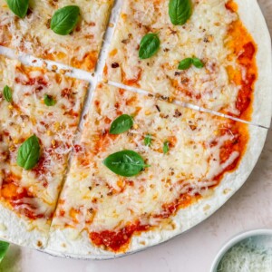 A close up overhead shot of a tortilla pizza. A ramekin of cheese is in the bottom right corner of the image.