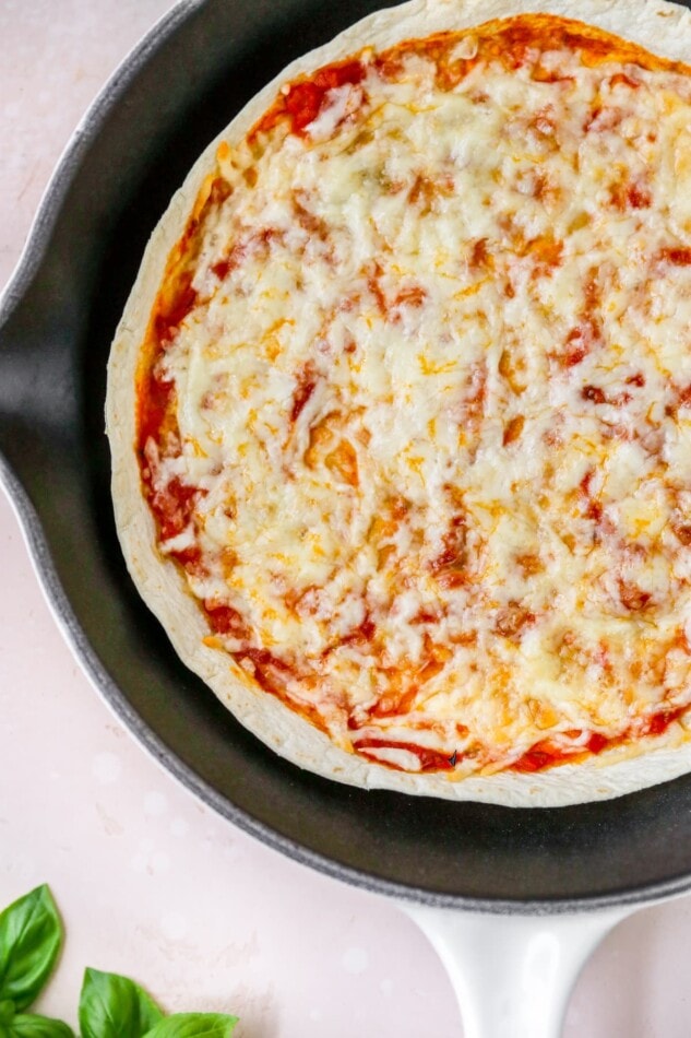 A finished tortilla pizza in a skillet after heating. The cheese is nice and melty.