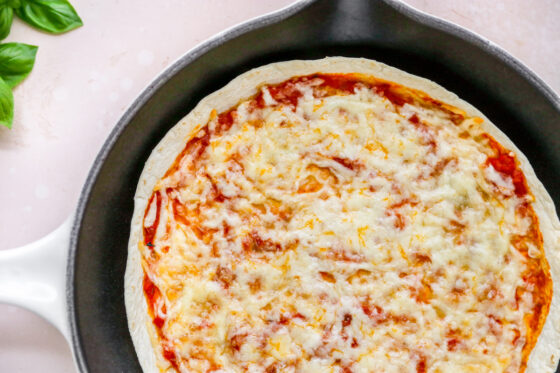 A finished tortilla pizza in a skillet after heating. The cheese is nice and melty.