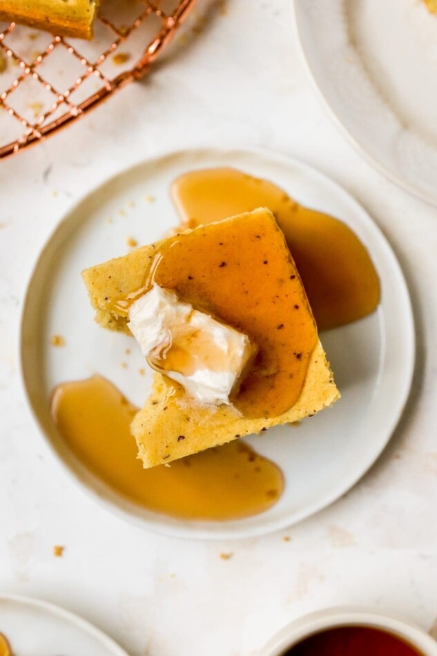 A closeup overhead photo of a piece of vegan cornbread with a bite missing. The cornbread is topped with a dollop of vegan butter and a drizzle of maple syrup.