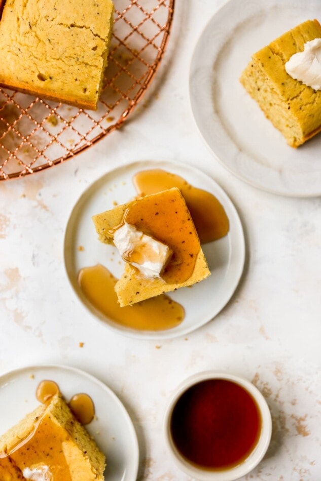 An overhead photo of a piece of vegan cornbread with a bite missing. The cornbread is topped with a dollop of vegan butter and a drizzle of maple syrup.