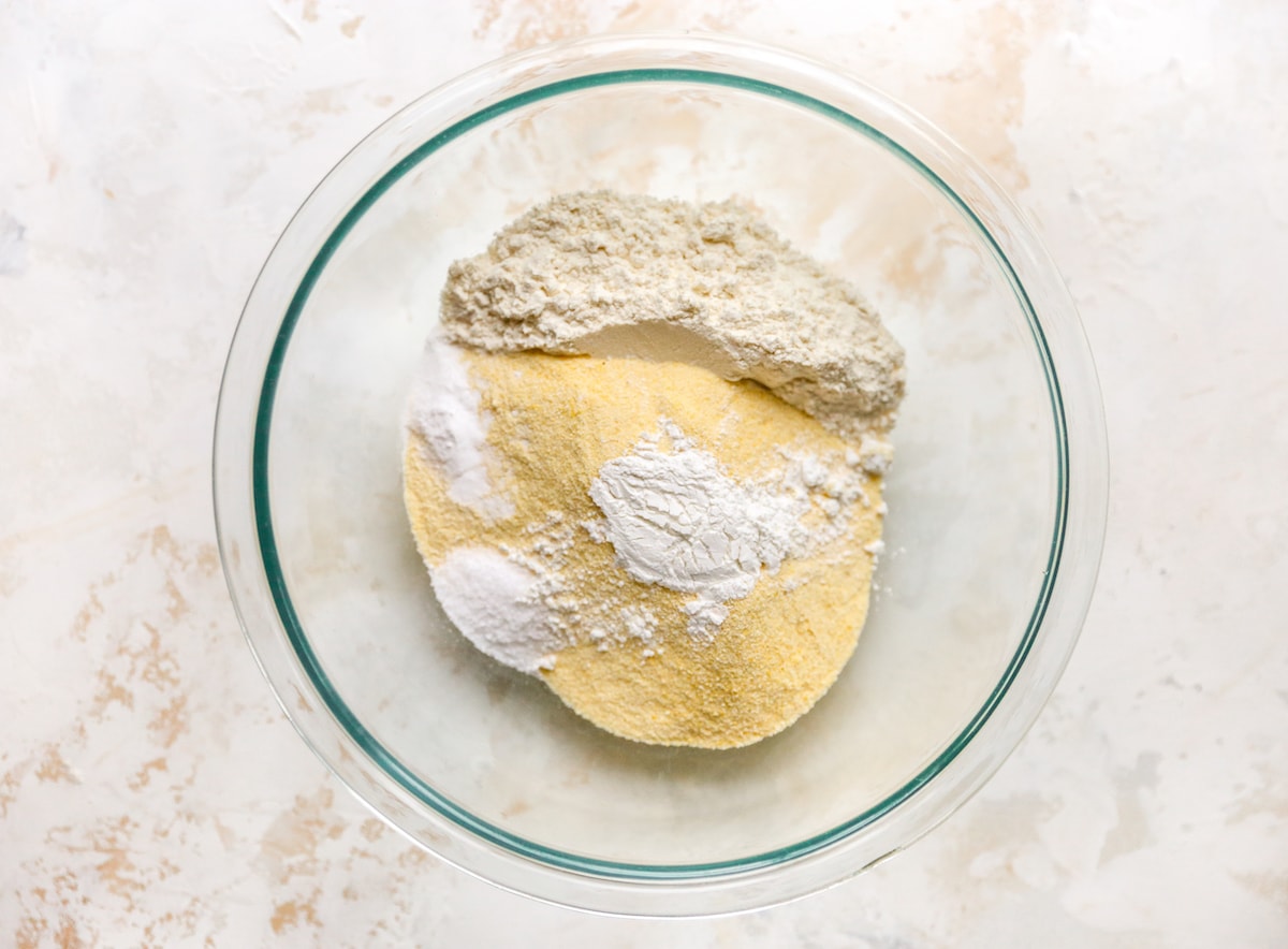 A glass mixing bowl with dry ingredients for vegan cornbread.