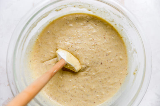 Wet and dry ingredients in a glass bowl mixed together. A spatula is resting on the edge of the bowl.