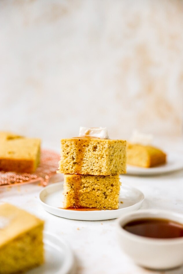 Two pieces of vegan cornbread stacked on top of each other topped with a pat of vegan butter being drizzled with maple syrup.