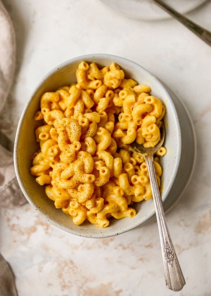 Overhead photo of a bowl of vegan mac and cheese sprinkled with pepper. A silver spoon rests inside the bowl.