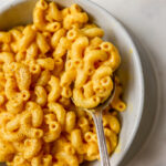 A spoonful of vegan mac and cheese being held overtop of a bowl filled with vegan mac and cheese.