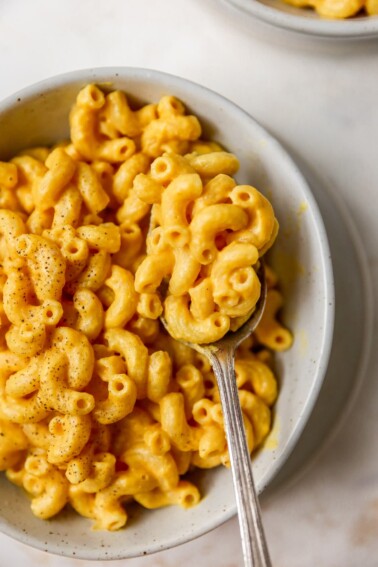 A spoonful of vegan mac and cheese being held overtop of a bowl filled with vegan mac and cheese.