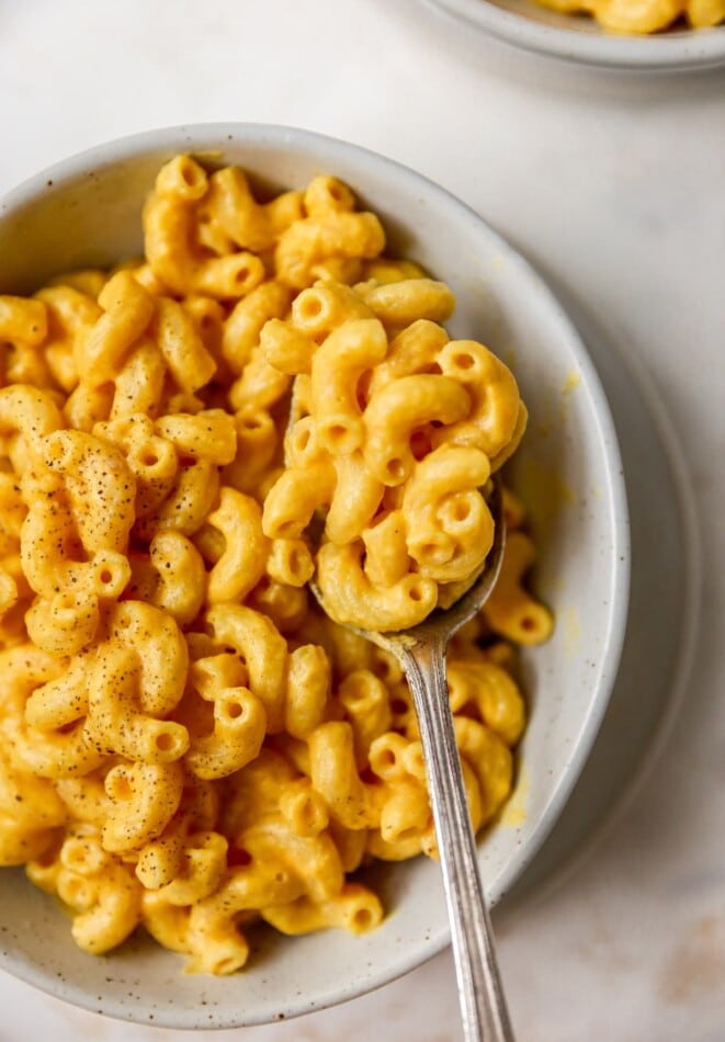 A spoonful of vegan mac and cheese being held overtop of a bowl filled with vegan mac and cheese.