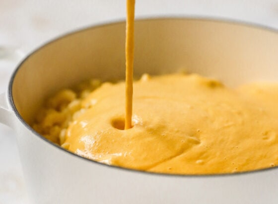 Vegan cheese being poured into a pot of cooked macaroni noodles.