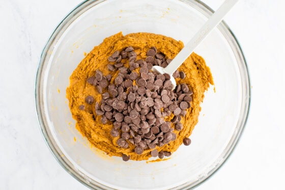 Chocolate chips added on top of the muffin mixture, not yet mixed in. A white spatula rests in the bowl.