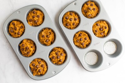 Two 6-muffin baking pans, with 10 of the cups filled with muffin batter, ready to be baked.