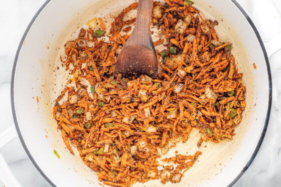 Seasonings were added and mixed into the shredded carrots and vegetables. A wooden spoon rests in the pot.