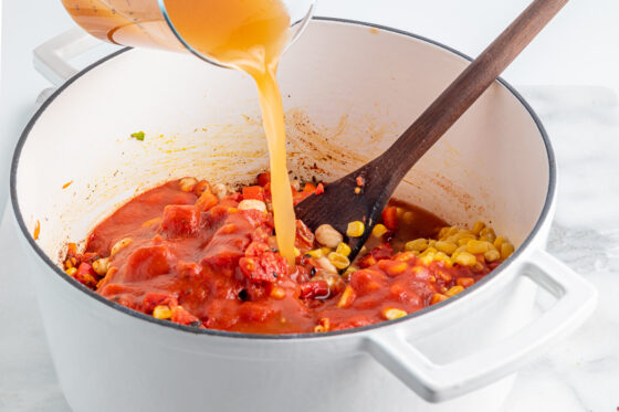 Vegetable broth is being poured from a measuring cup into the pot of chili.