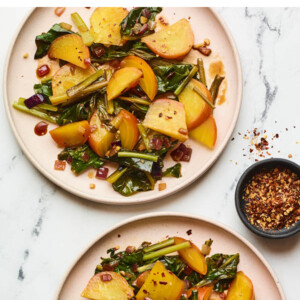 Two plates with beets and greens and a small ramekin of red pepper flakes.