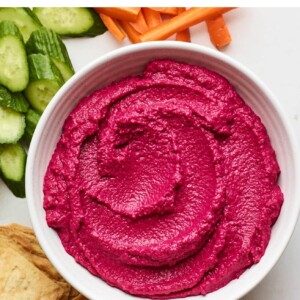 Overhead photo of a bowl of beet hummus surrounded by various veggies for dipping.