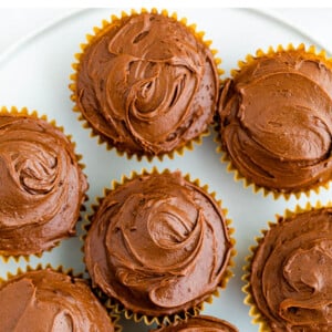 An overhead photo looking at cupcakes wrapped in paper wrapping on a plate topped with healthy chocolate frosting.