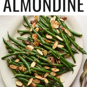 An overhead photo of a serving dish holding green beans almondine. A serving fork and spoon lay next to the dish.