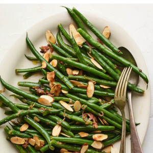 An overhead photo of a serving dish holding green beans almondine. A serving fork and spoon lay on the side of the dish.