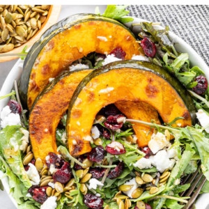 An overhead photo of a bowl of kale topped with 3 slices of roasted kabocha squash and scattered with dried cranberries, pumpkin seeds and feta. A fork rests in the bowl.