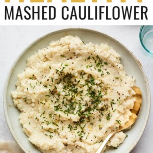A bowl of mashed cauliflower topped with chives. A serving spoon rests inside the bowl.