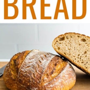 A loaf of sourdough bread on a wooden cutting board with a loaf that has been cut in half leaning against it.