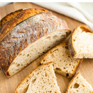 A loaf of sourdough bread sliced open on a wooden cutting board with 2 slices cut in half scattered in front of the loaf.