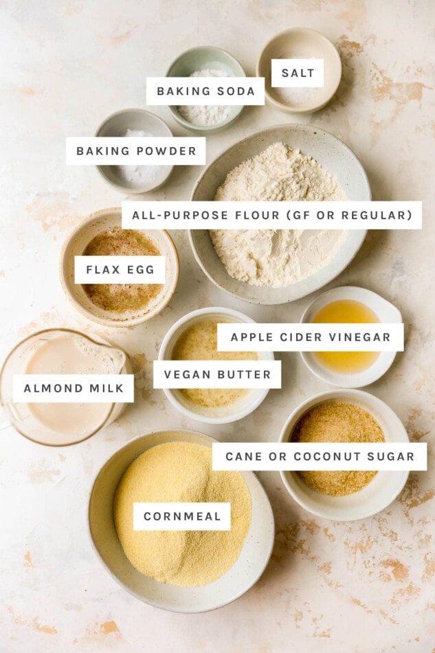 Ingredients measured out in little bowls to make vegan cornbread: salt, baking soda, baking powder, flour, flax egg, apple cider vinegar, vegan butter, almond milk, sugar and cornmeal.