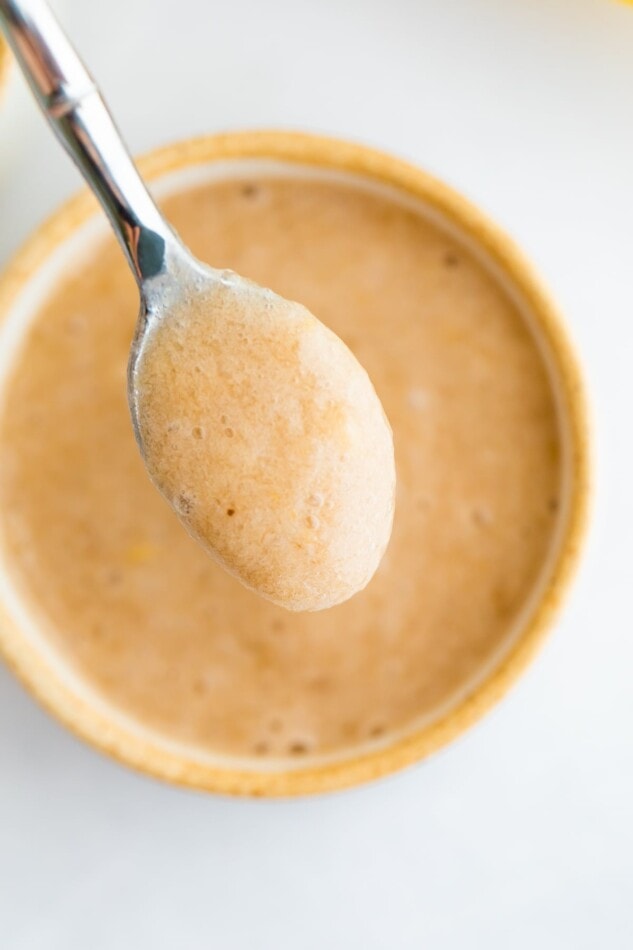 An overhead photo of a small dish with banana puree. A spoonful of puree is being held up by a spoon.