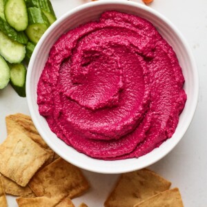 Overhead photo of a bowl of beet hummus surrounded by various veggies for dipping.
