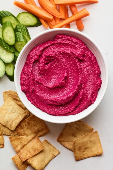 Overhead photo of a bowl of beet hummus surrounded by various veggies for dipping.