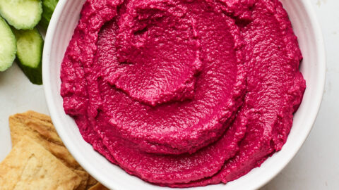 Overhead photo of a bowl of beet hummus surrounded by various veggies for dipping.