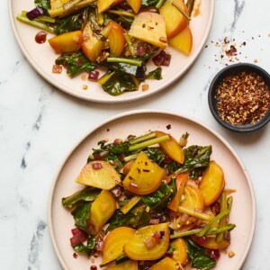 Two plates with beets and greens and a small ramekin of red pepper flakes.