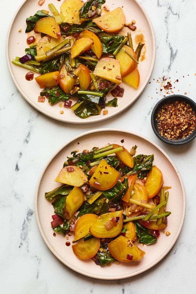 Two plates with beets and greens and a small ramekin of red pepper flakes.