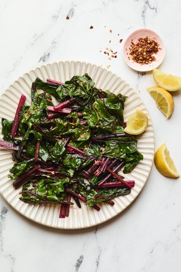 A plate of beet greens with a few lemon wedges and red pepper flakes.