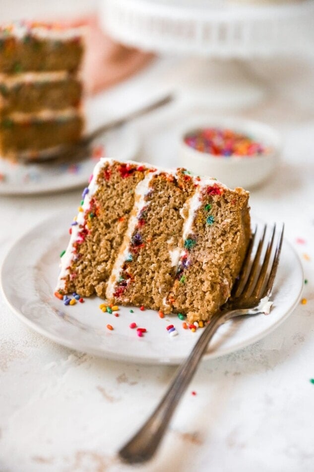 A slice of birthday cake on a plate, laying on its side.